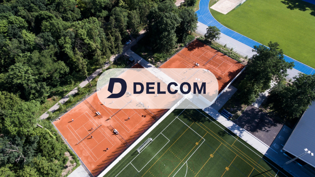 Aerial view of outdoor tennis courts, a soccer field, and surrounding greenery on a sunny day.